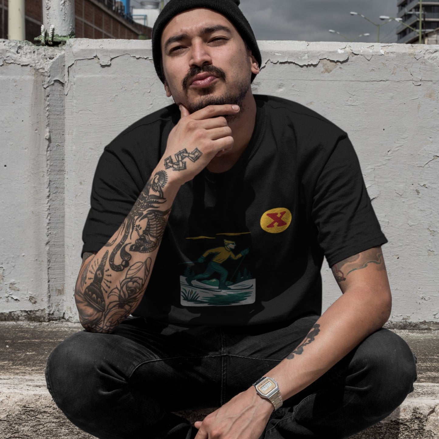 Man sitting against a concrete wall wearing the Made in Canada cross country skiing T shirt in black