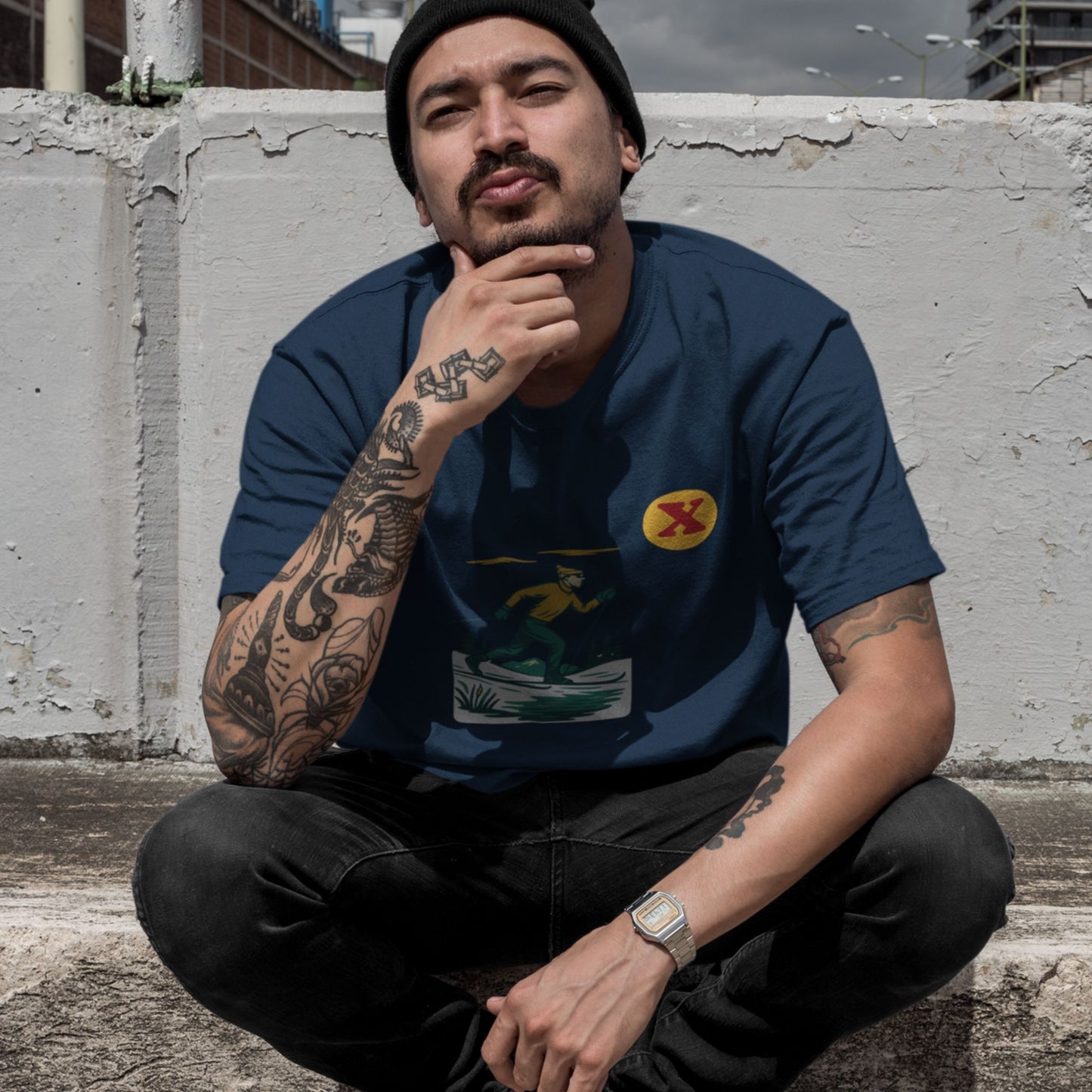 Man sitting against a concrete wall wearing the Made in Canada cross country skiing T shirt in Navy colour