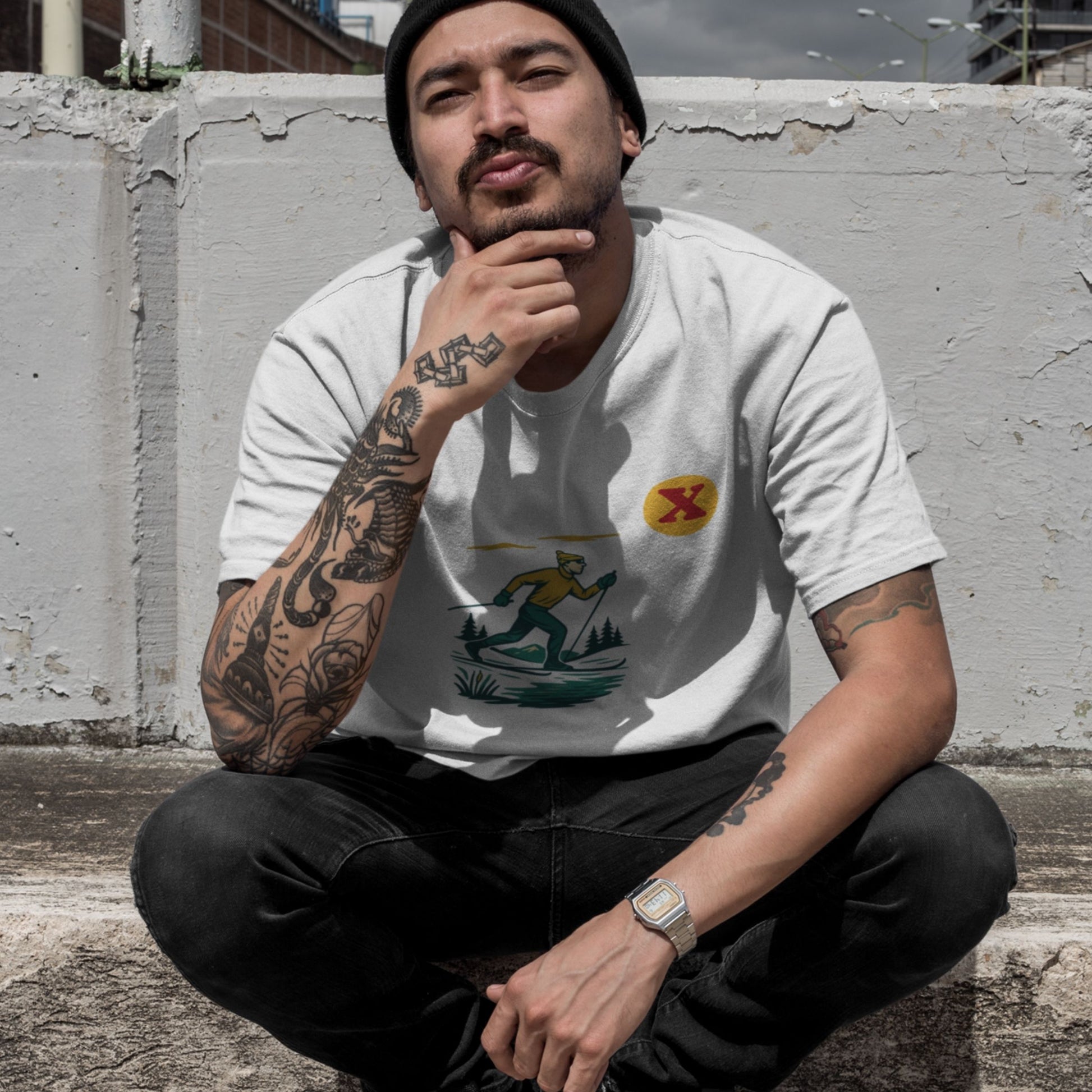 Man sitting against a concrete wall wearing the Made in Canada cross country skiing T shirt in white