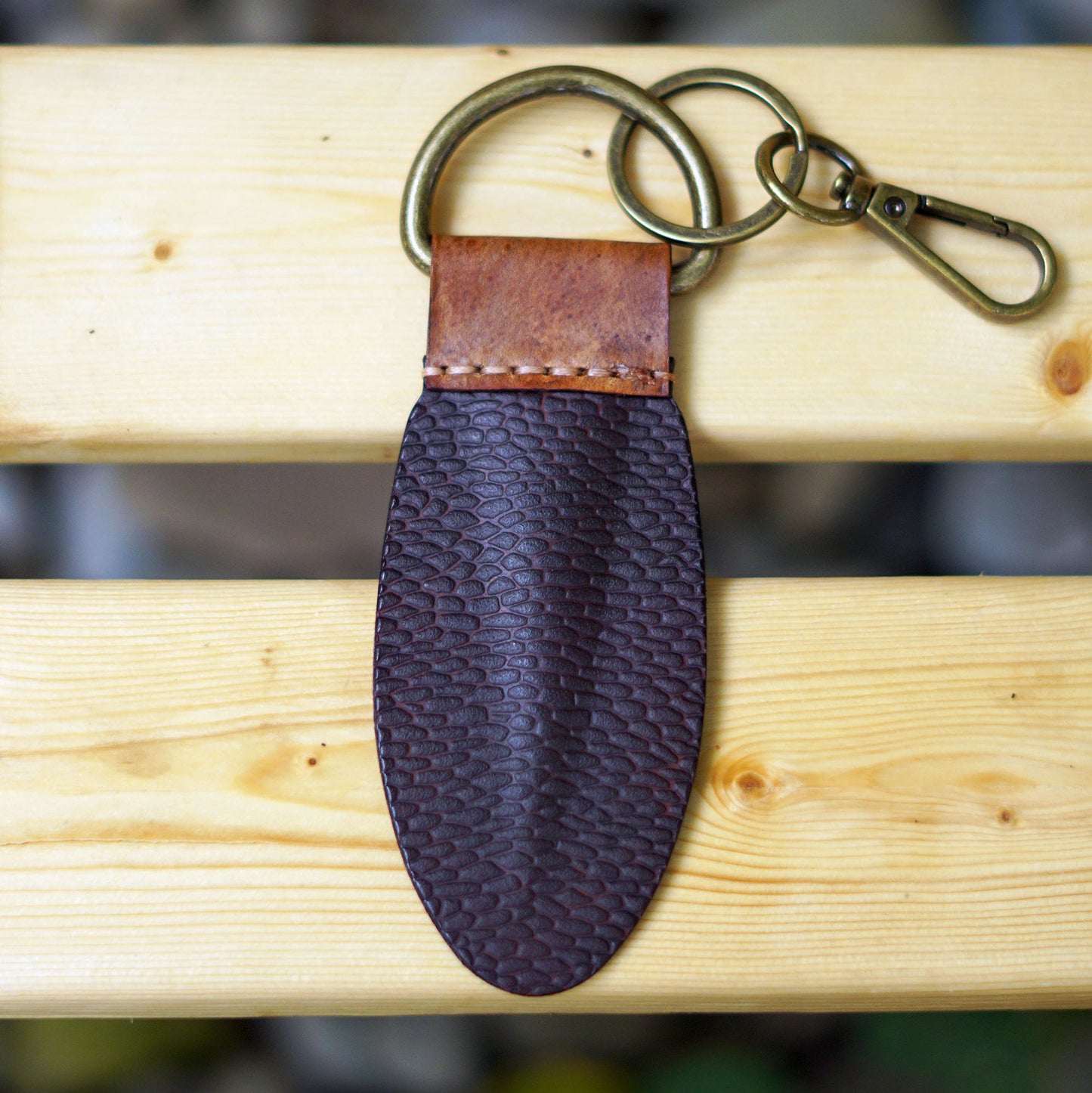 Back side of the BeaverTag a handmade Canadian leather keychain inspired by the beaver's tail placed on a wooden bench