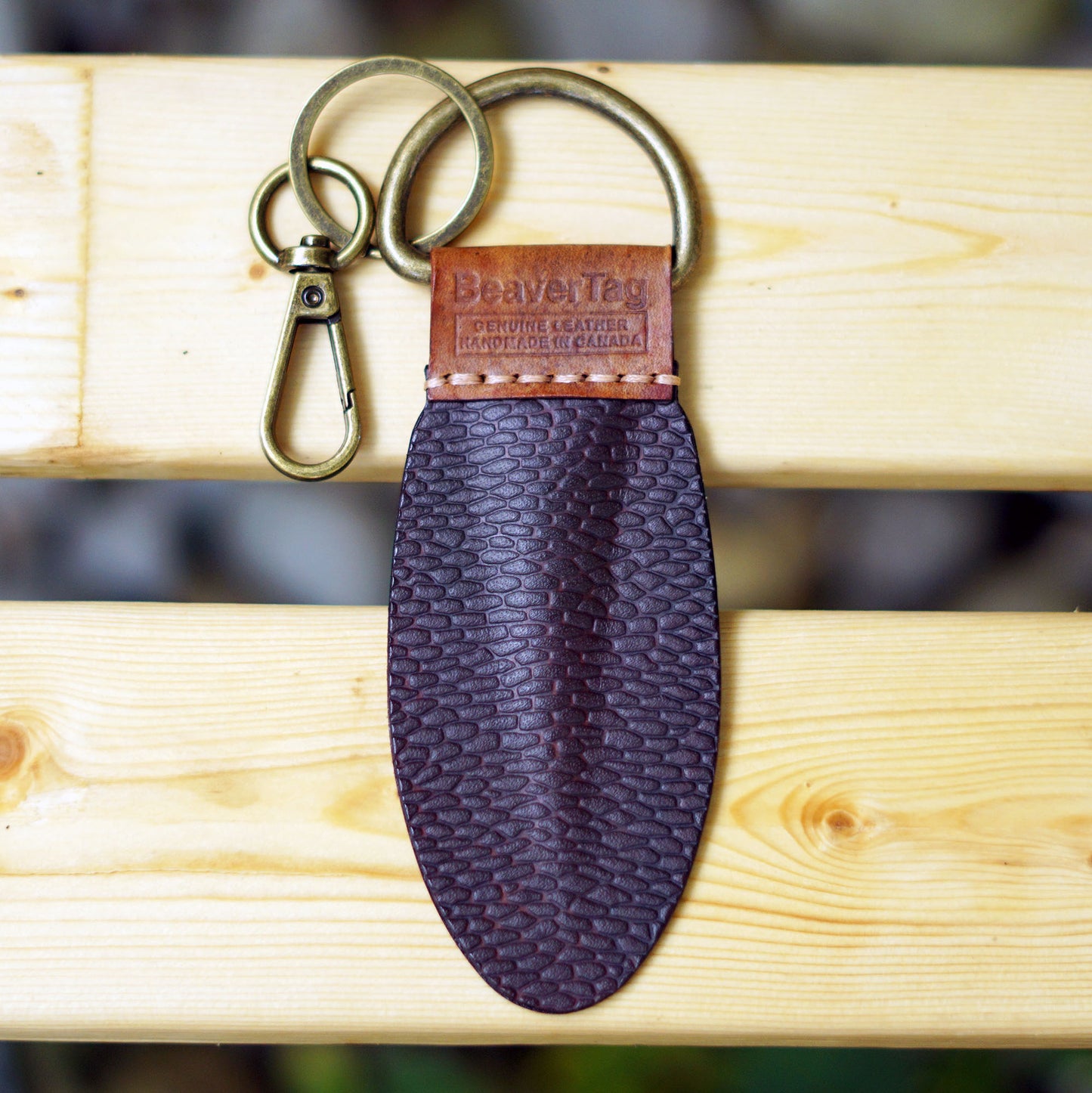 BeaverTag a handmade Canadian leather keychain inspired by the beaver's tail placed on a wooden bench