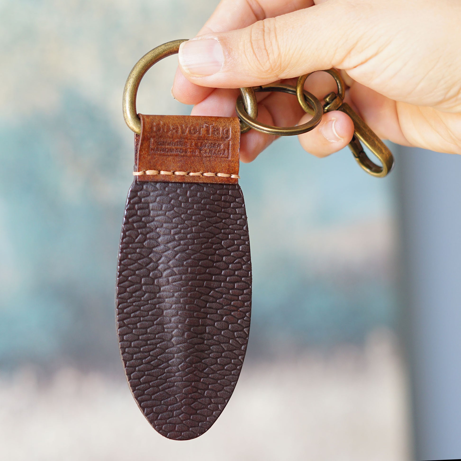BeaverTag - canadian leather keychain with brass ring held by a hand against a blurred background